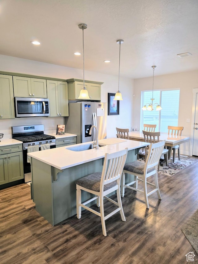 kitchen with appliances with stainless steel finishes, green cabinetry, a breakfast bar area, dark wood finished floors, and an island with sink