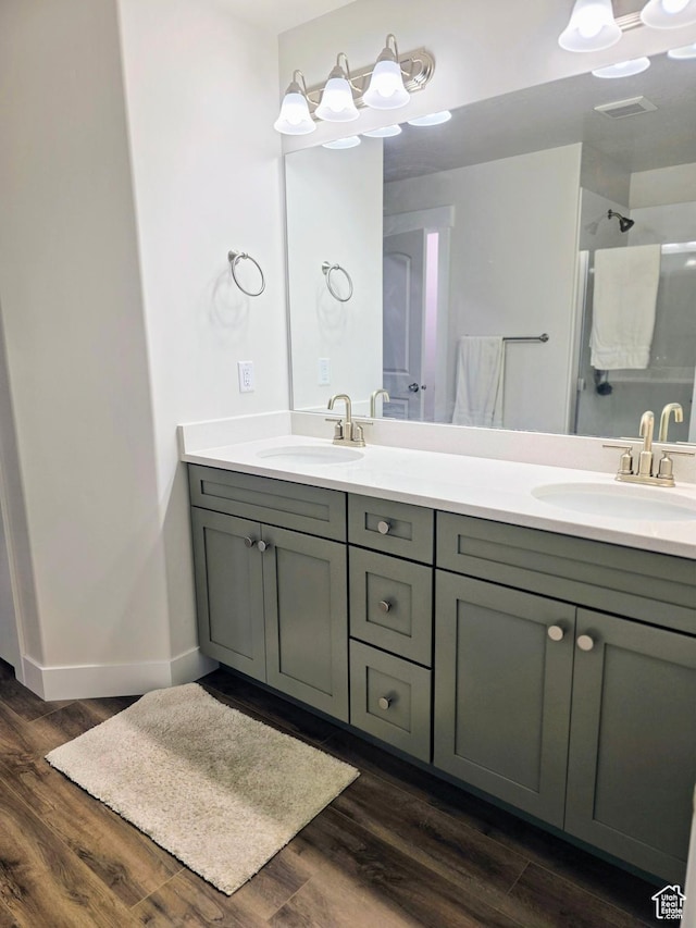 full bath with double vanity, wood finished floors, a shower, and baseboards