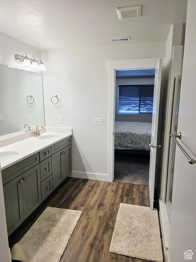 ensuite bathroom with wood finished floors, double vanity, a textured ceiling, and baseboards