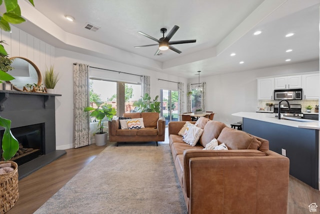living room featuring wood finished floors, recessed lighting, ceiling fan, a raised ceiling, and a large fireplace