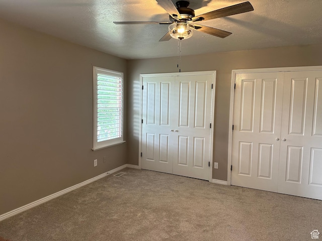unfurnished bedroom with multiple closets, carpet flooring, baseboards, and a textured ceiling