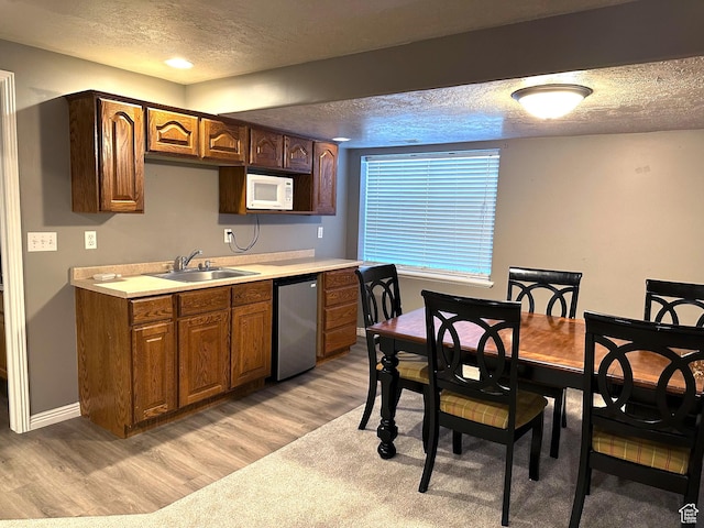 kitchen featuring a sink, a textured ceiling, white microwave, light wood-style flooring, and light countertops