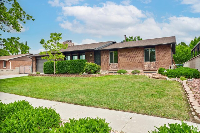 single story home with a chimney, brick siding, a front yard, driveway, and a garage