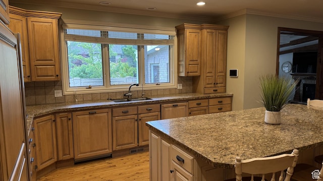 kitchen featuring a sink, light wood-style floors, decorative backsplash, ornamental molding, and a breakfast bar area