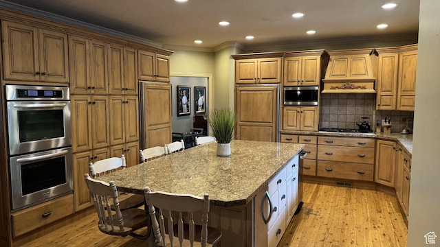 kitchen featuring appliances with stainless steel finishes, premium range hood, a kitchen breakfast bar, light wood finished floors, and crown molding