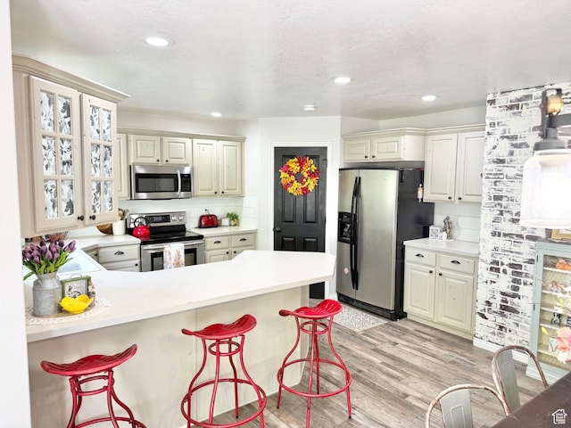 kitchen with stainless steel appliances, a kitchen bar, a peninsula, light countertops, and light wood finished floors
