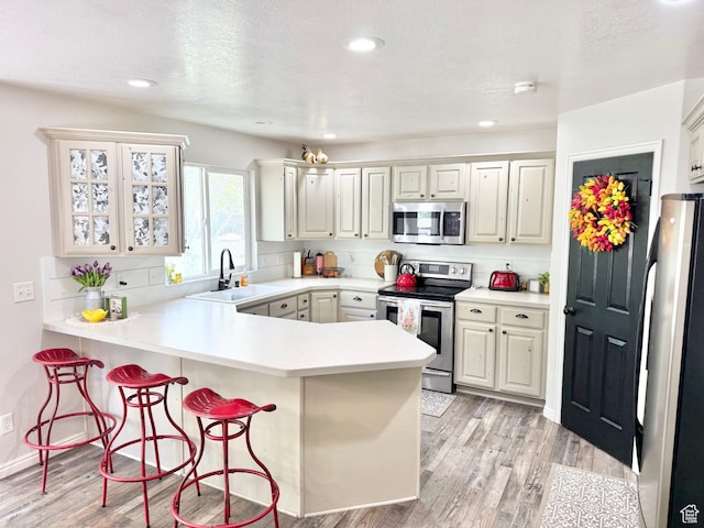 kitchen with appliances with stainless steel finishes, a sink, a peninsula, a kitchen bar, and light wood-style floors