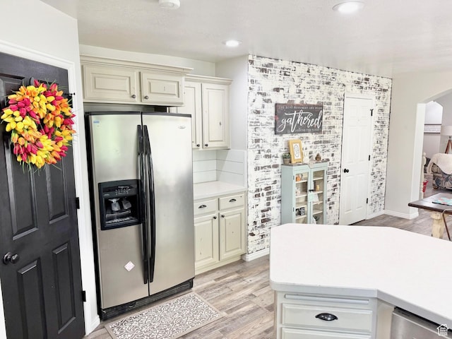 kitchen with stainless steel fridge with ice dispenser, light countertops, arched walkways, light wood-style flooring, and cream cabinets