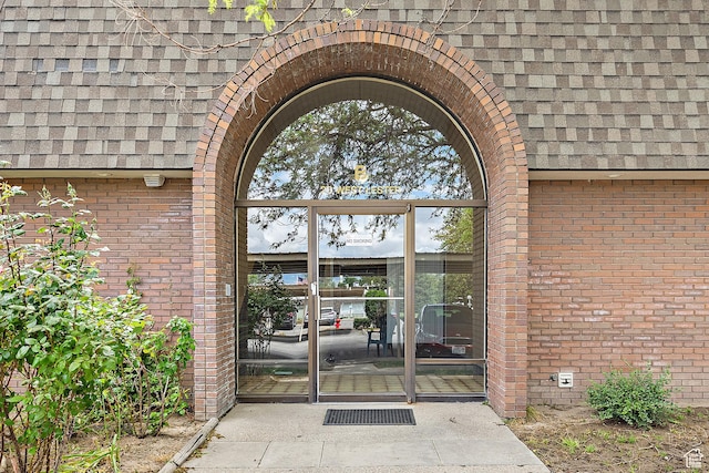 doorway to property with roof with shingles and brick siding