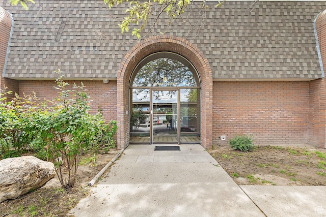 view of exterior entry featuring a shingled roof and brick siding