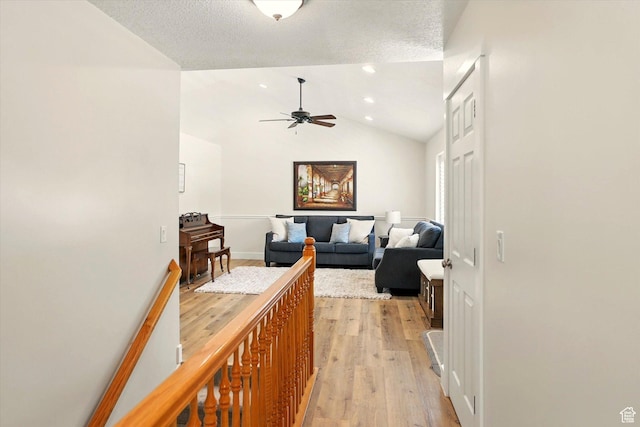 corridor featuring light wood-style flooring, lofted ceiling, and a textured ceiling