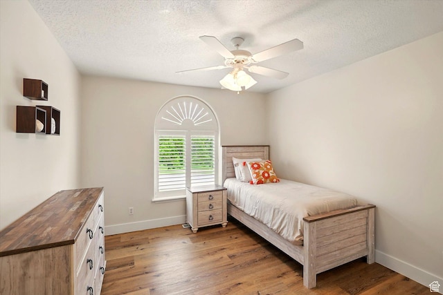 bedroom with baseboards, light wood-type flooring, a textured ceiling, and ceiling fan