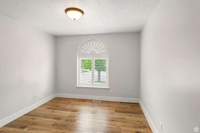 spare room with a textured ceiling, baseboards, and wood finished floors