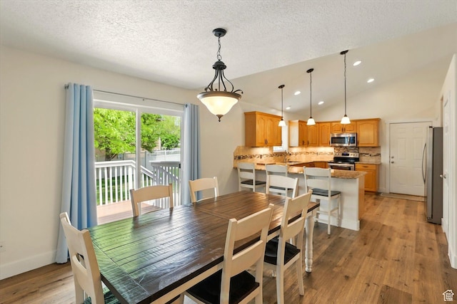 dining area featuring light wood-style flooring, a textured ceiling, recessed lighting, vaulted ceiling, and baseboards