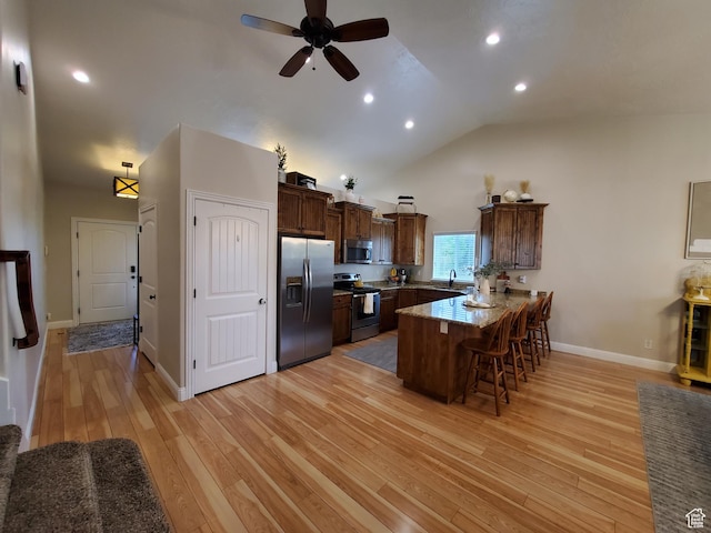 kitchen with appliances with stainless steel finishes, a peninsula, a breakfast bar, light wood-style floors, and ceiling fan
