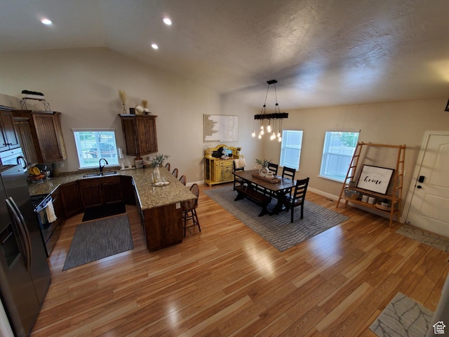 kitchen with a peninsula, light wood-style floors, a breakfast bar area, a sink, and vaulted ceiling