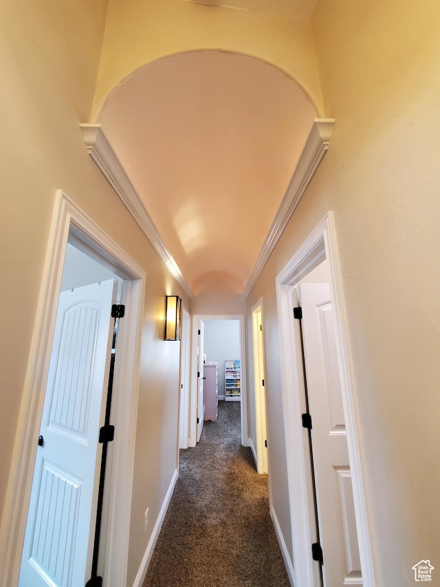 hallway featuring crown molding, dark carpet, and baseboards