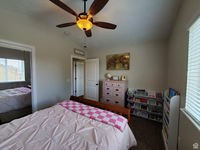 bedroom featuring multiple windows, vaulted ceiling, dark carpet, and a ceiling fan