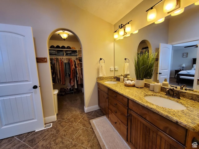 ensuite bathroom with double vanity, vaulted ceiling, tile patterned floors, a spacious closet, and baseboards
