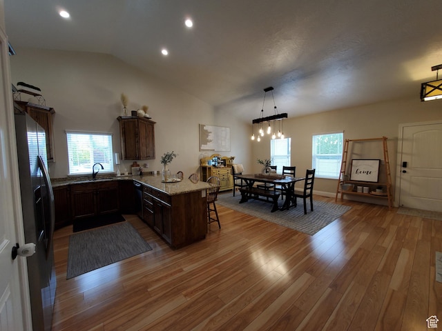kitchen with stainless steel refrigerator with ice dispenser, a kitchen bar, a sink, a peninsula, and light wood-style floors