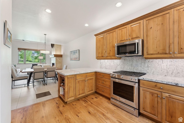 kitchen featuring stainless steel appliances, a peninsula, decorative backsplash, light stone countertops, and brown cabinetry