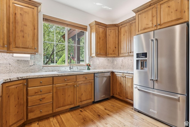 kitchen featuring appliances with stainless steel finishes, light wood-type flooring, backsplash, light stone countertops, and a sink