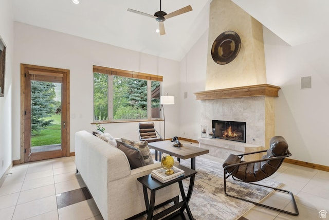 living area with high vaulted ceiling, baseboards, light tile patterned floors, a high end fireplace, and ceiling fan