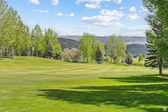 view of property's community with golf course view, a mountain view, and a lawn
