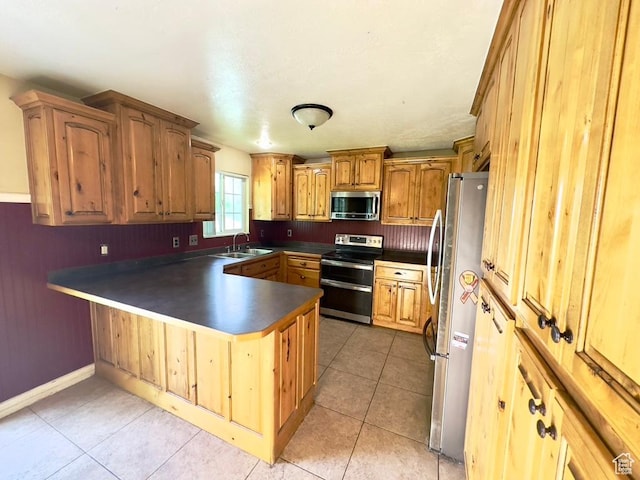 kitchen with appliances with stainless steel finishes, a sink, a peninsula, dark countertops, and light tile patterned floors