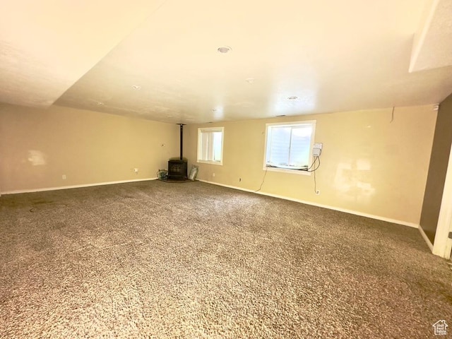 carpeted empty room featuring a wood stove and baseboards