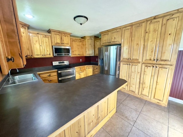 kitchen with appliances with stainless steel finishes, a sink, dark countertops, and a peninsula