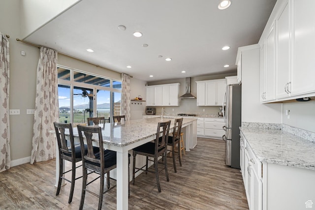 kitchen with wall chimney range hood, appliances with stainless steel finishes, recessed lighting, wood finished floors, and a kitchen breakfast bar