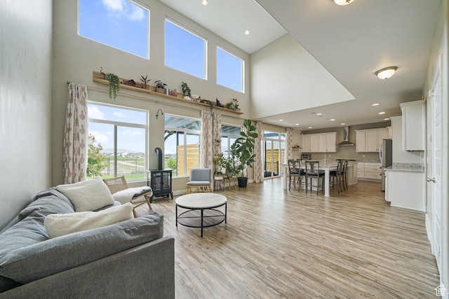 living room with a high ceiling, light wood-type flooring, a wood stove, and recessed lighting
