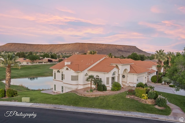 mediterranean / spanish home featuring a water and mountain view, a front lawn, a garage, and stucco siding