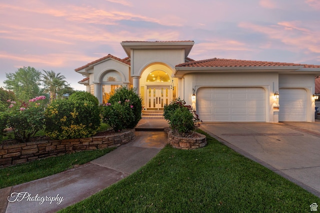 mediterranean / spanish-style house with a garage, concrete driveway, a tile roof, and stucco siding