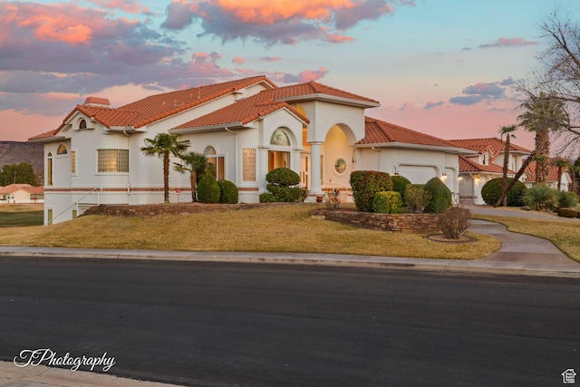 mediterranean / spanish-style home featuring an attached garage, a tiled roof, stucco siding, a front yard, and driveway
