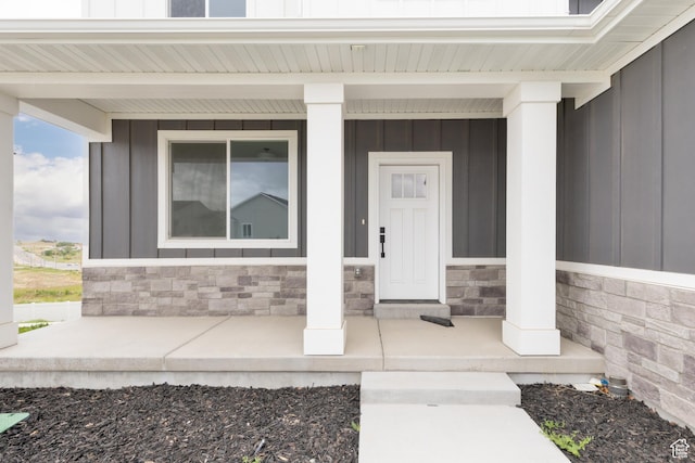 view of exterior entry featuring covered porch, board and batten siding, and stone siding