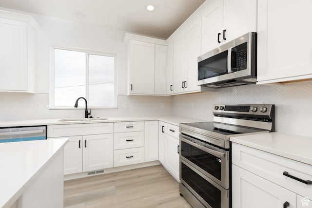 kitchen with appliances with stainless steel finishes, tasteful backsplash, white cabinetry, light countertops, and recessed lighting