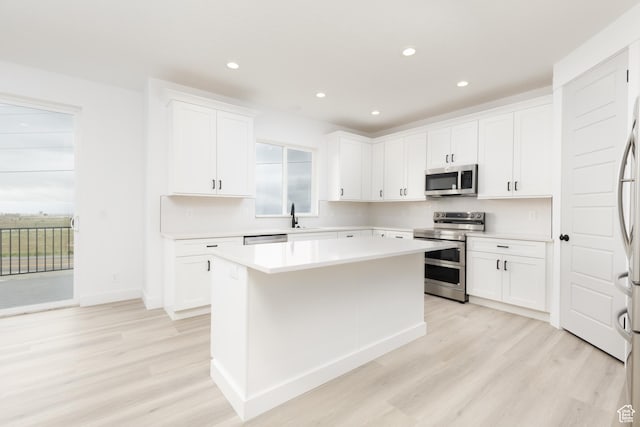 kitchen featuring appliances with stainless steel finishes, light wood-type flooring, light countertops, a center island, and white cabinetry