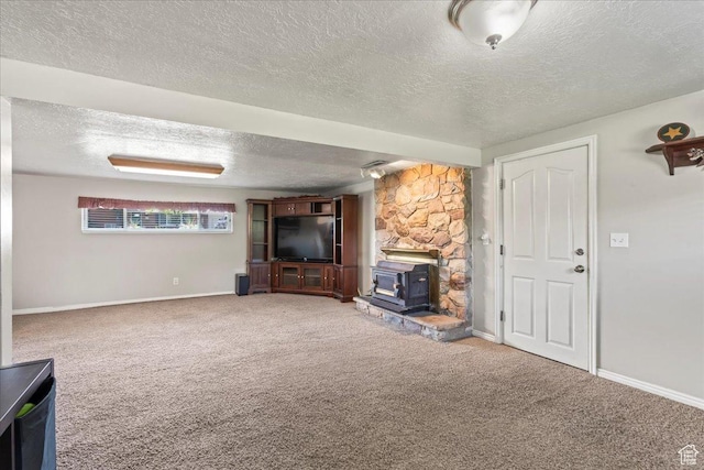 unfurnished living room featuring a wood stove, a textured ceiling, carpet floors, and baseboards