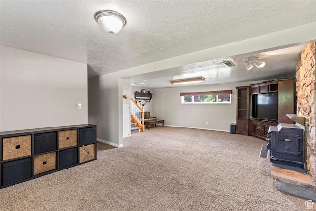 unfurnished living room featuring a wood stove, stairs, carpet floors, a textured ceiling, and baseboards