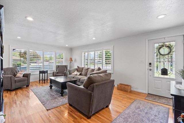 living room featuring a textured ceiling, light wood finished floors, ornamental molding, baseboards, and recessed lighting