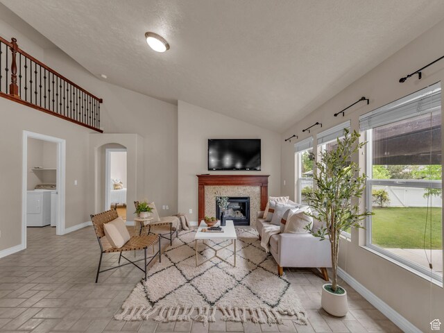 living room featuring independent washer and dryer, baseboards, a glass covered fireplace, arched walkways, and high vaulted ceiling