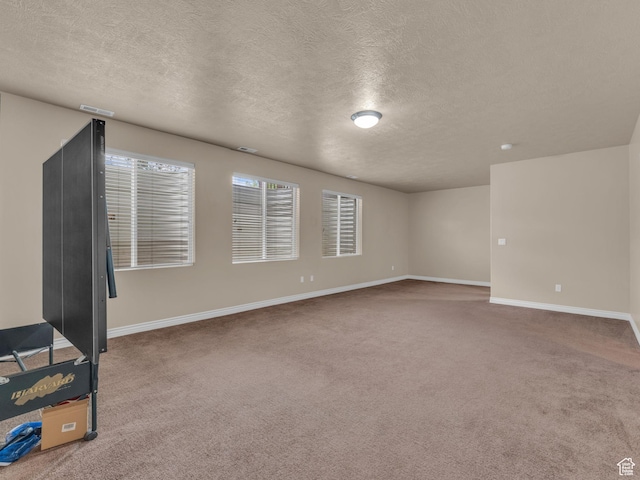 spare room with a textured ceiling, carpet, and baseboards