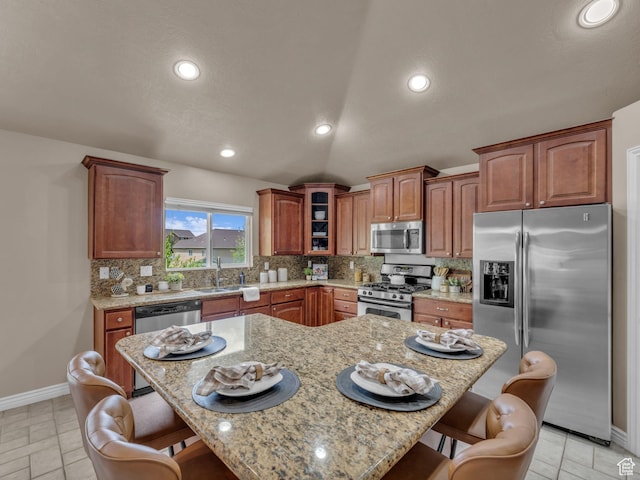kitchen featuring stainless steel appliances, a kitchen breakfast bar, backsplash, light stone countertops, and baseboards