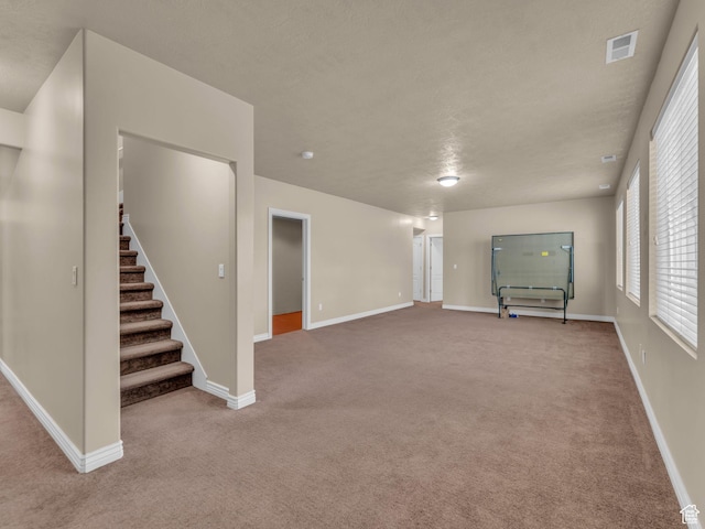 unfurnished living room featuring carpet floors, stairway, baseboards, and a textured ceiling
