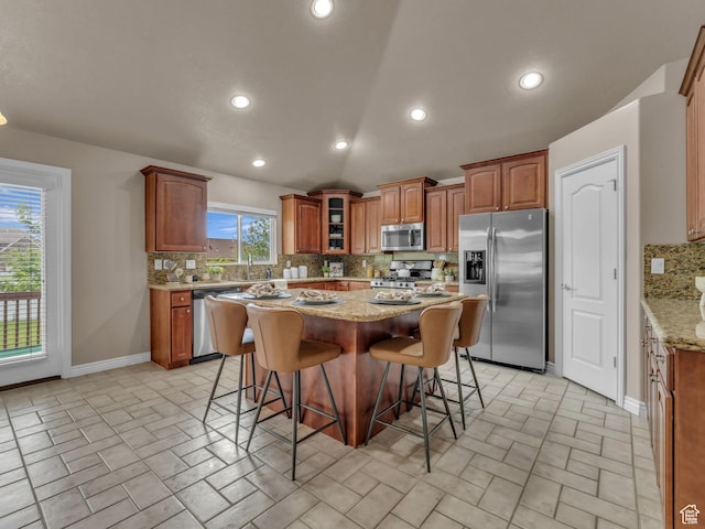 kitchen with appliances with stainless steel finishes, tasteful backsplash, a kitchen bar, light stone counters, and a kitchen island