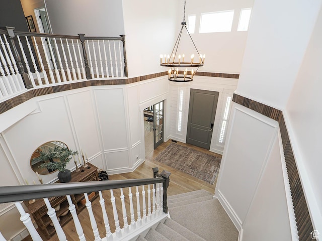 foyer featuring a decorative wall, stairs, a chandelier, a high ceiling, and light wood-style floors