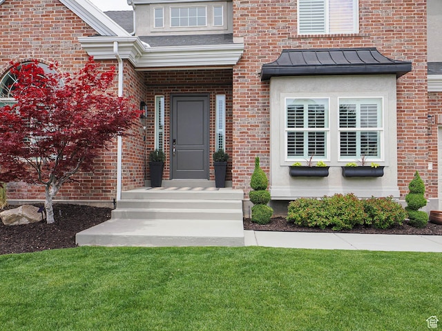 property entrance with a standing seam roof, a yard, and brick siding
