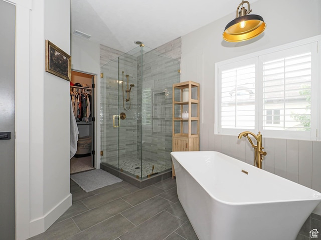 full bath featuring a stall shower, a walk in closet, a freestanding tub, and tile patterned floors